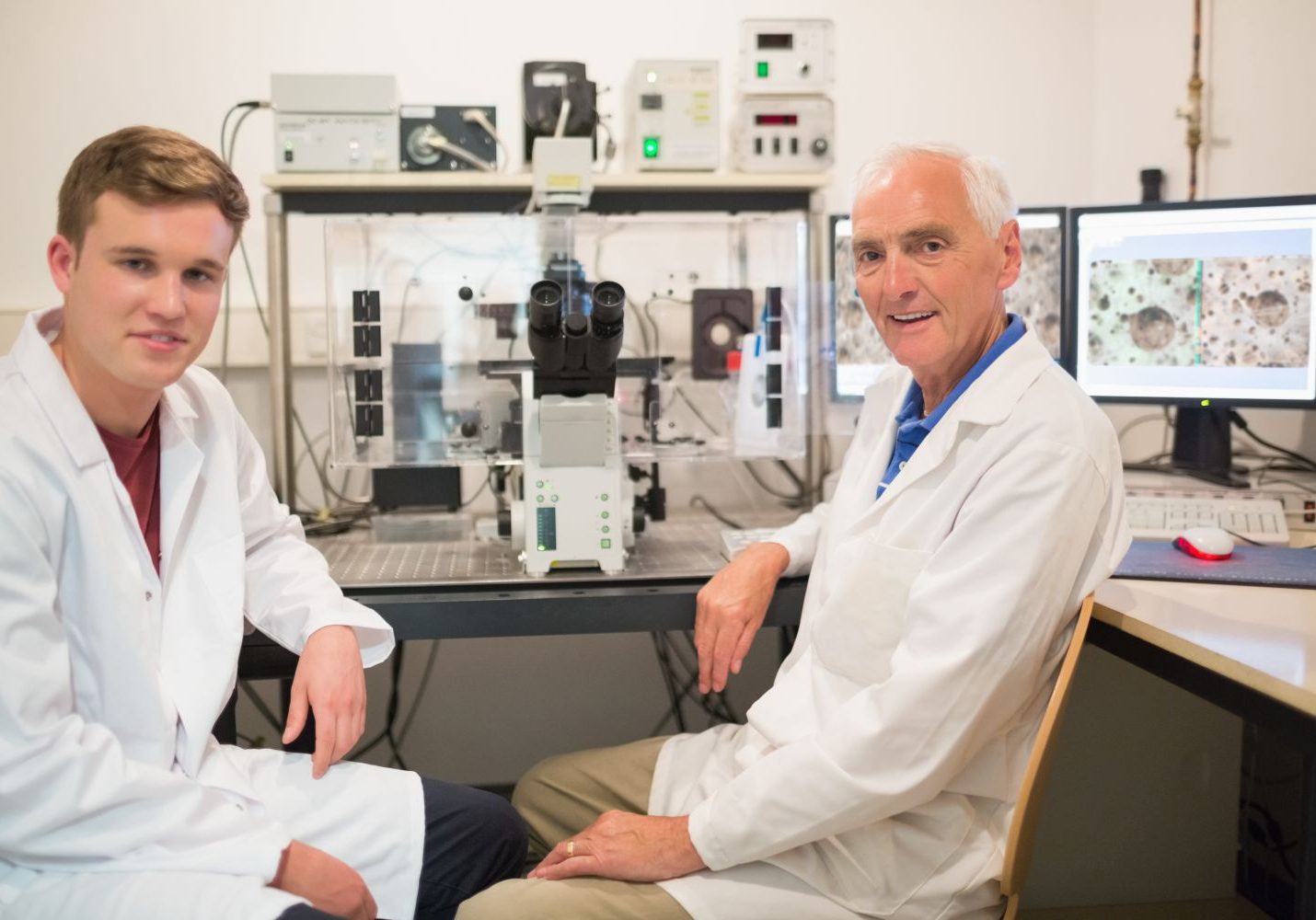Biochemist using large microscope and computer with student at the university